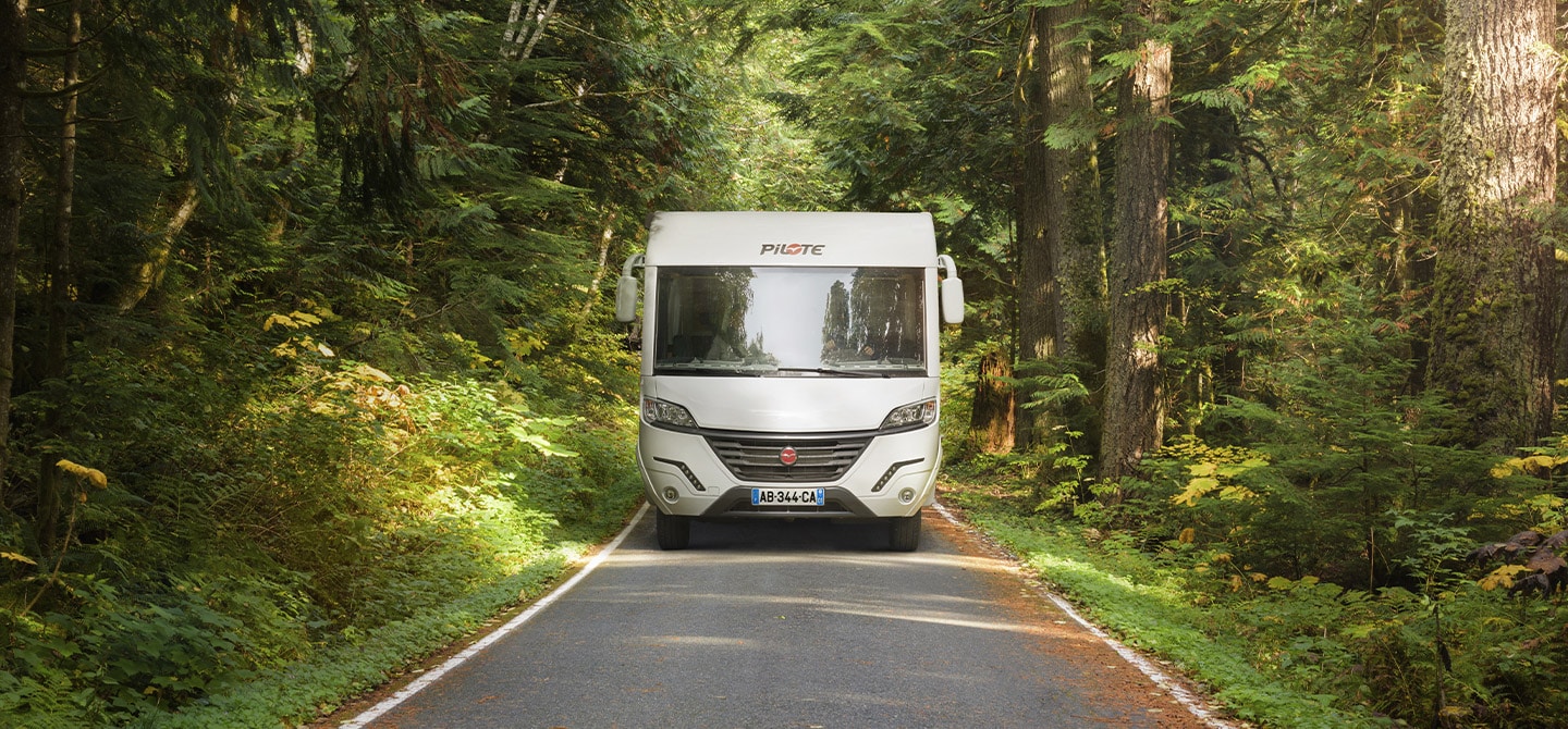 Camping-car intégral Pilote sur une route au milieu d'une forêt dense.