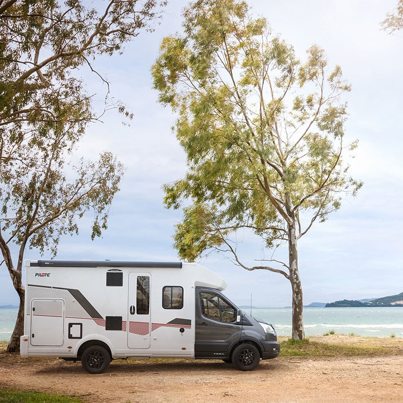Camping-car profilé étroit Pilote sur un chemin à l'arrêt, la mer au second plan.