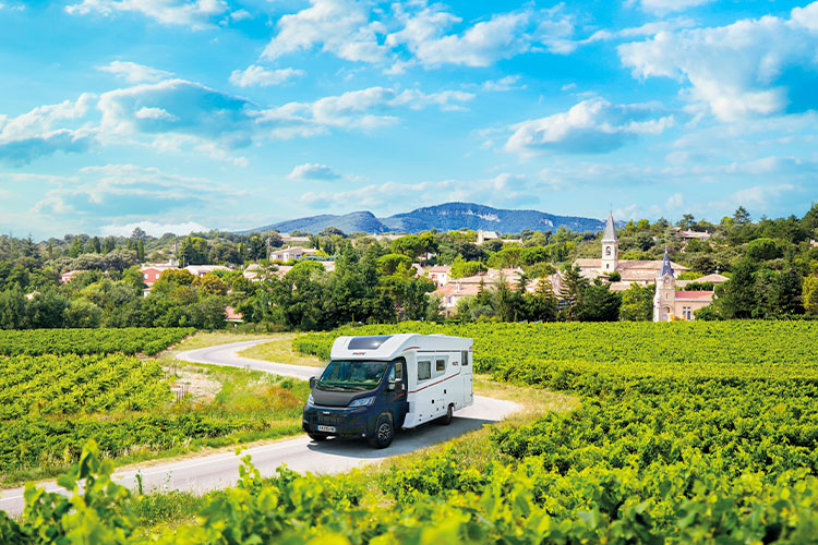 camping-car profilé Pilote avec la cabine avant noire roulant sur une route entouré de vignes